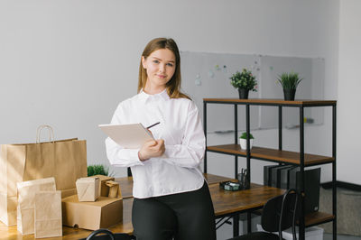 A cute girl in the office makes notes in a notebook next to eco packages on the table