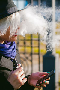 Young woman using mobile phone while smoking at park
