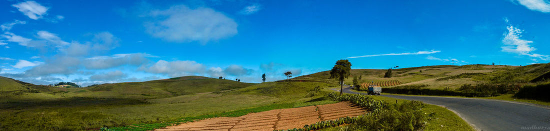 Panoramic view of road amidst landscape against blue sky