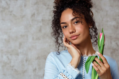 Portrait of young woman holding camera against wall