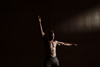 Sportsman with hand raised standing against gray wall during sunset