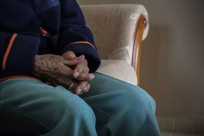 Midsection of person sitting with hands clasped on sofa at home