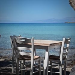 Empty chairs and table by sea against sky