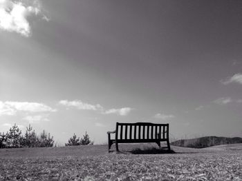 Empty bench on field against sky