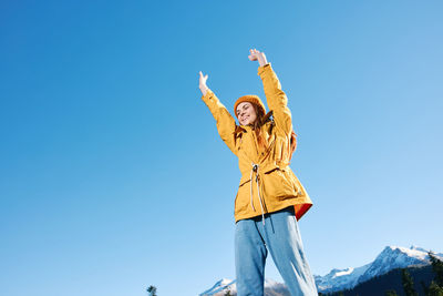 Young woman with arms raised standing against clear blue sky