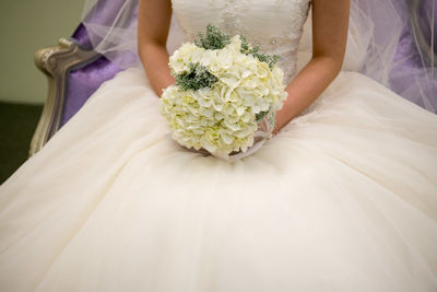 Midsection of bride holding bouquet while sitting on chair