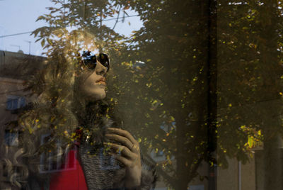 Beautiful young woman wearing sunglasses while looking through glass window