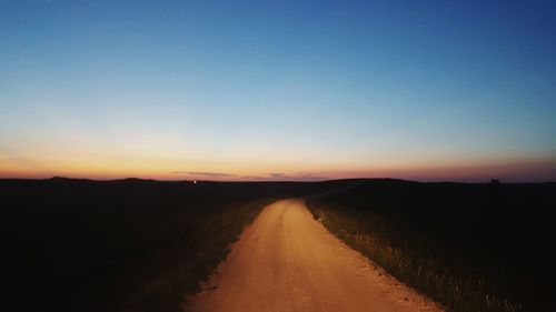 Dirt road along landscape against clear sky during sunset