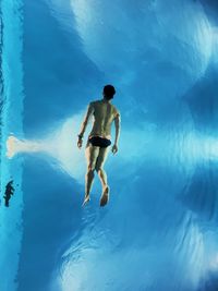 Rear view of shirtless man swimming in pool