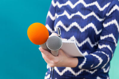 Close-up of woman holding microphone and note pad against colored background