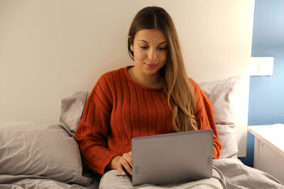 Beautiful woman using laptop while sitting on bed at home