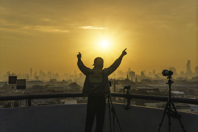 Full length of man standing by cityscape against sky during sunset