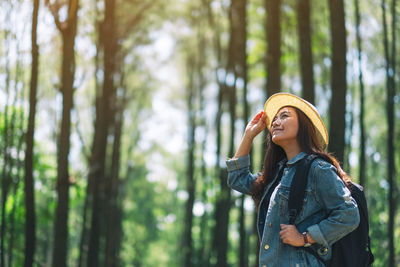 Young woman looking away while standing on tree in forest