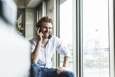 Happy casual young man listening to music with headphones at the window