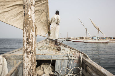 Rear view of man on boat sailing in sea against clear sky