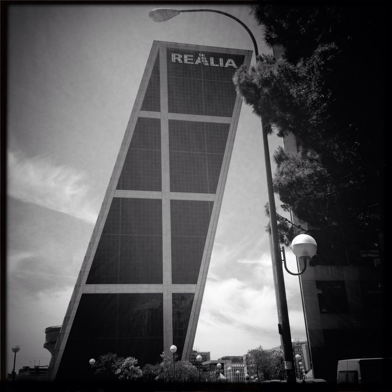 architecture, low angle view, building exterior, built structure, transfer print, tree, auto post production filter, sky, city, tower, tall - high, building, modern, office building, skyscraper, street light, day, outdoors, no people, tall