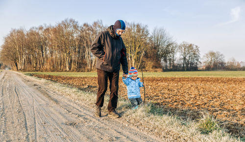 Grandfather and granddaughter holding hands while walking on land