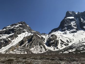 Low angle view of snowcapped mountains against clear blue sky