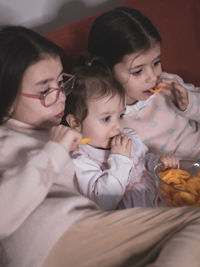 Three girls are watching a movie sitting on the couch.