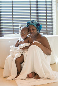 Portrait of mother and son with towels sitting in bathroom