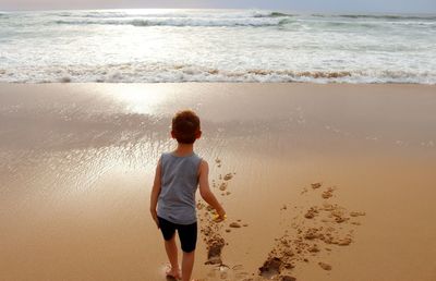 The red-haired boy stands with his back to the camera and looks out over the atlantic ocean. 