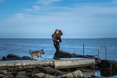 Man with dog standing on rock by sea against sky