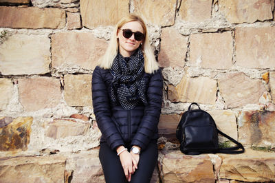 Portrait of smiling young woman sitting against stone wall