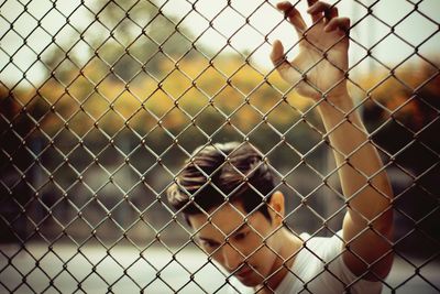 Close-up of man seen through chainlink fence