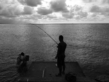 Silhouette man fishing in sea against cloudy sky