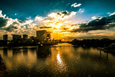 Scenic view of river by buildings against sky during sunset