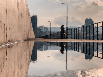 Reflection of woman standing on swimming pool against sky