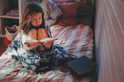 Young woman reading book on bed at home