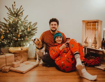 Portrait of smiling couple with dog sitting by christmas tree at home