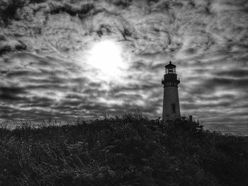Lighthouse on field against cloudy sky