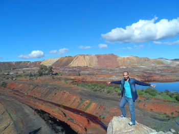 Man standing with arms outstretched on rock at mountain against sky