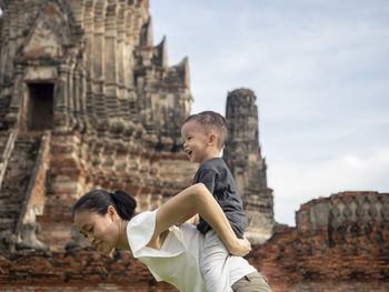 Side view of mother carrying son on back against ancient temple