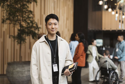 Portrait of confident young male entrepreneur holding diary while standing at convention center
