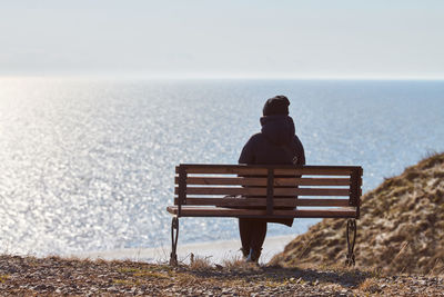 Rear view of man sitting on beach against clear sky