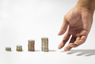 Cropped image of hand holding coin stack against white background