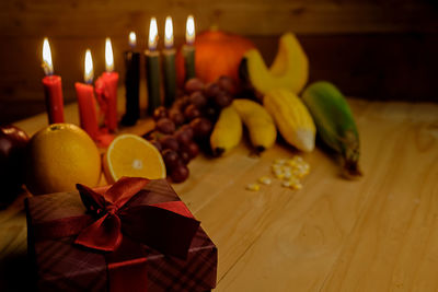 Close-up of gift with fruits and illuminated candles on table