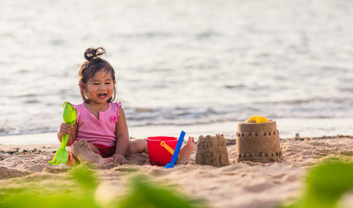 Full length of girl sitting on beach making castle on beach