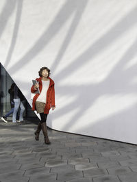 Curly woman in red duffle coat is walking. adult student with laptop. freelancer with device. 