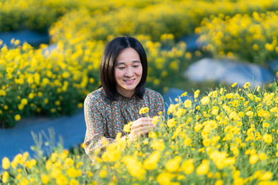 Portrait of smiling young woman with yellow flowers in field