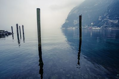 Wooden posts in sea against sky