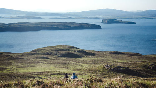 Scenic view of sea and mountains against sky on the isle of skye. three men sitting 