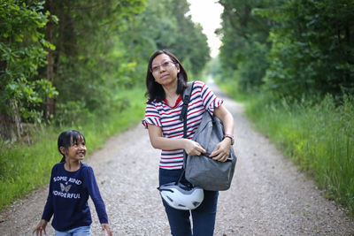 Full length of woman on road with daughter  walking carrying bag with bicycle helmet