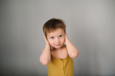 European toddler child 3 years old  yellow overalls covers his ears with his hands on monochromatic