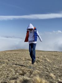 Rear view of man walking on field against sky