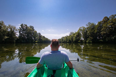 Rear view of man sitting on lake against sky