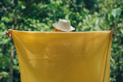 Person holding yellow scarf while standing against trees